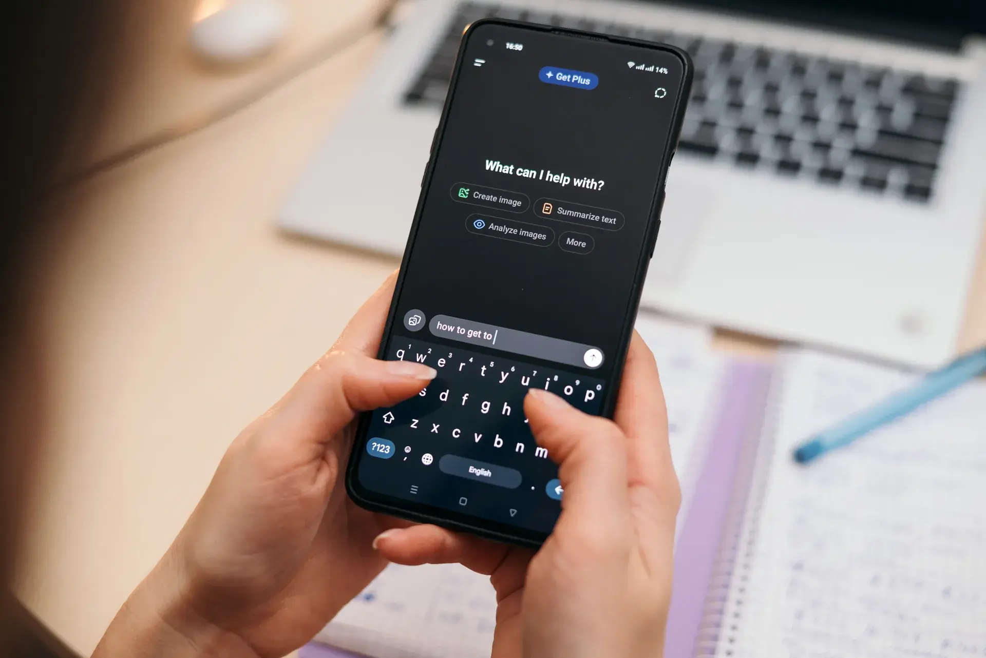 Hands typing a prompt into an AI assistant on a phone, beside a laptop and notes