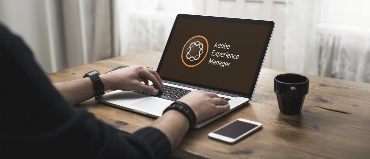 A person typing on a laptop displaying the Adobe Experience Manager logo at a wooden desk